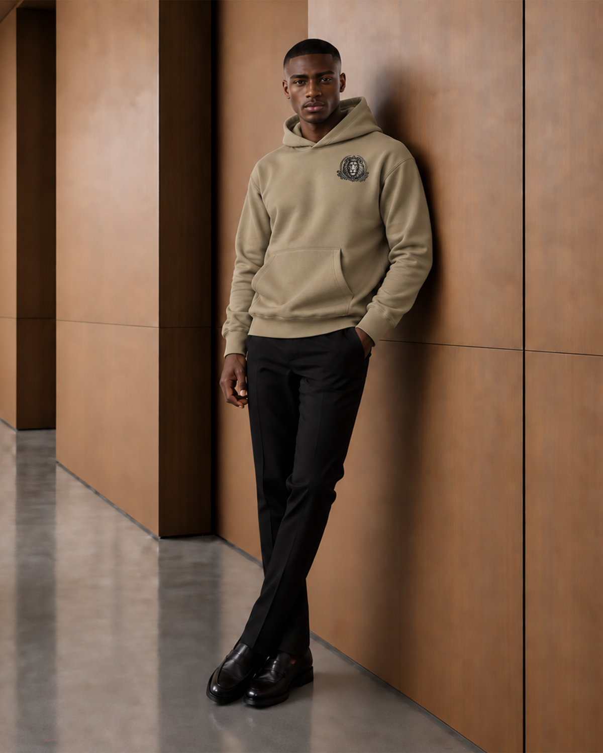 Relaxed editorial view of a model in the sand Strong & Courageous hoodie with a small crowned lion crest at the chest.