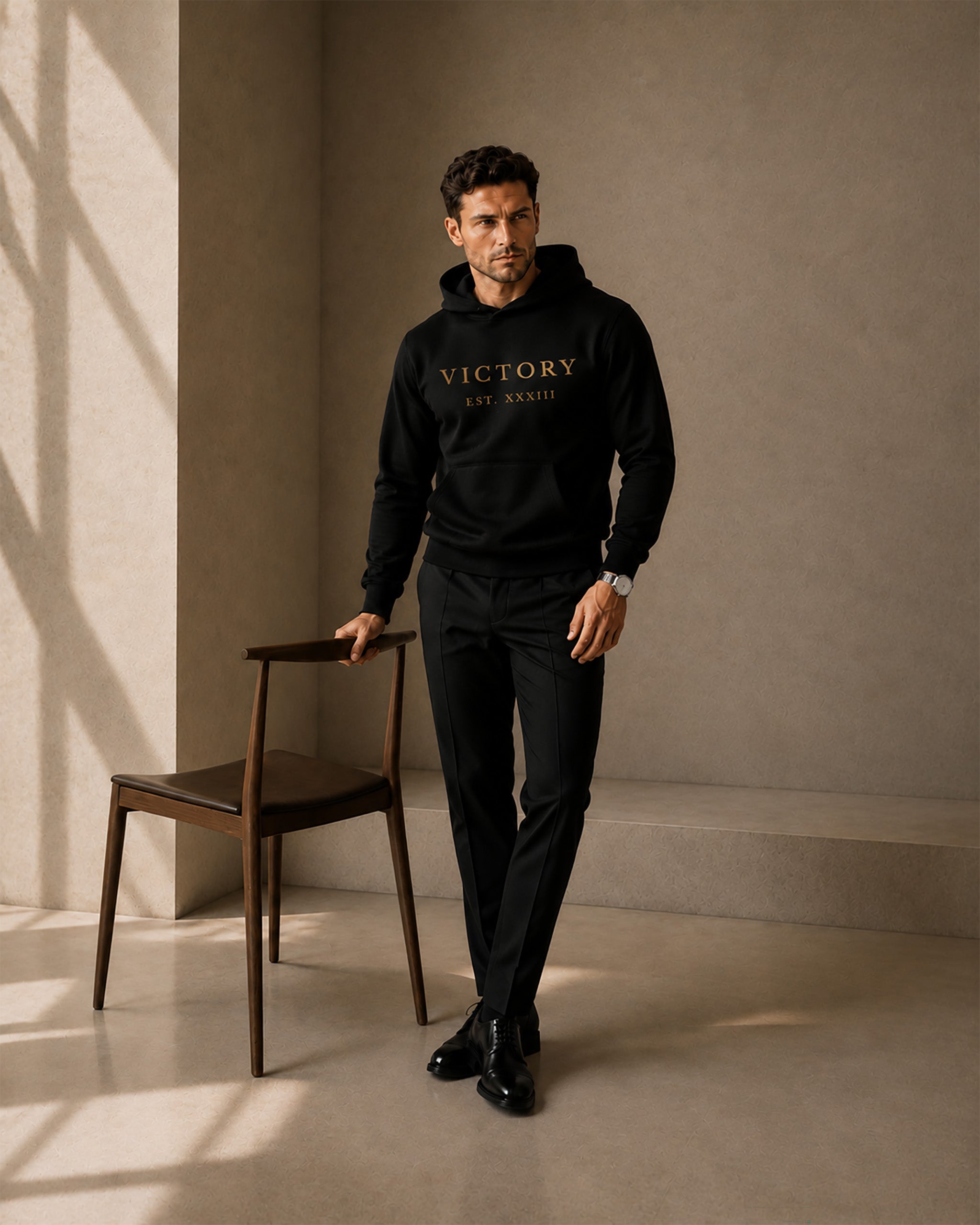 Man wearing a black hoodie with 'VICTORY' text, standing in a minimalistic room.