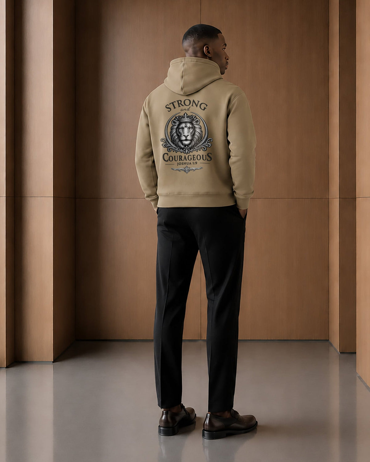 Back view of a model wearing the Strong & Courageous sand hoodie, featuring the large crowned lion illustration and Joshua 1:9 design.