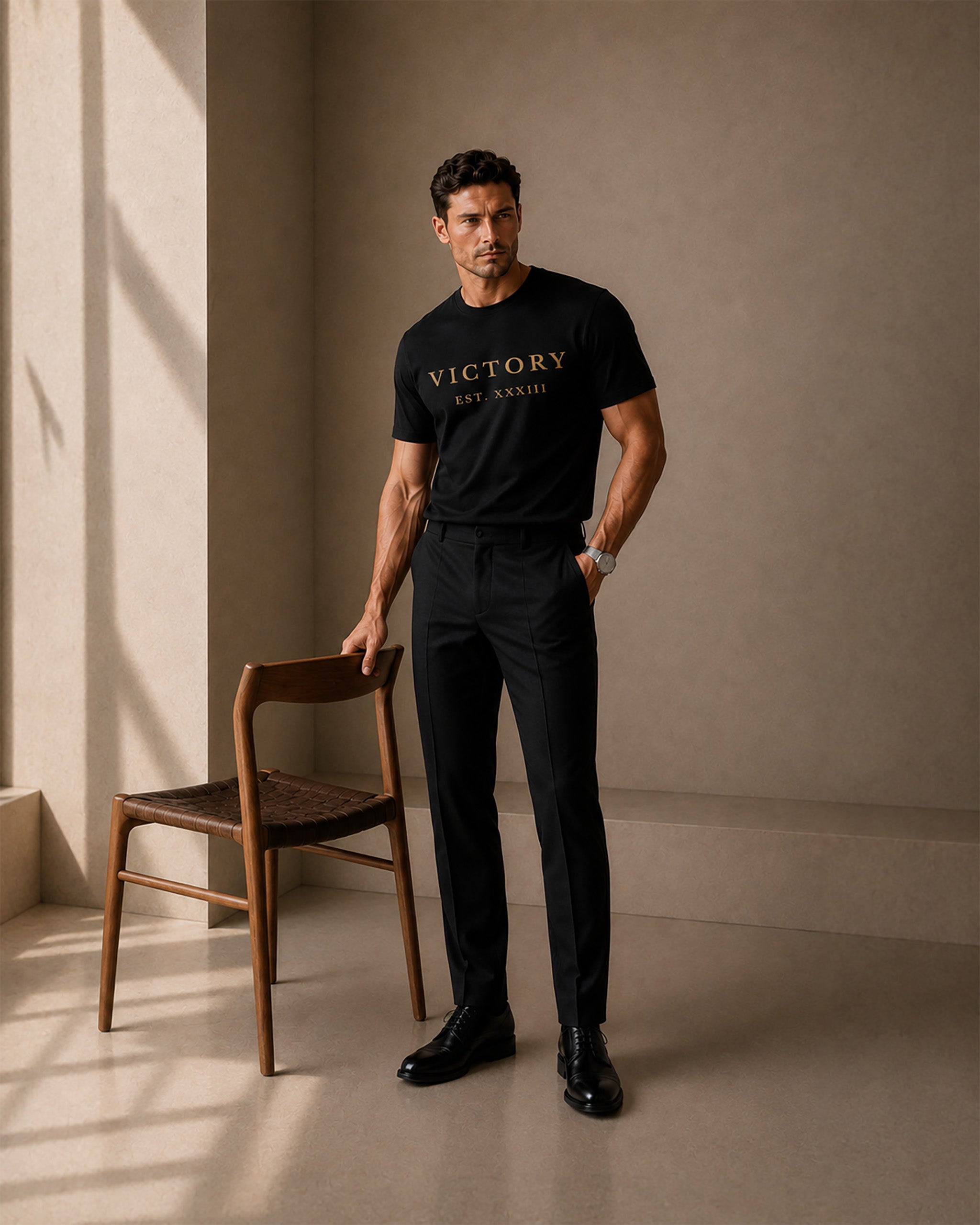 Man wearing a black t-shirt with 'VICTORY' text, standing in a room with a wooden chair.
