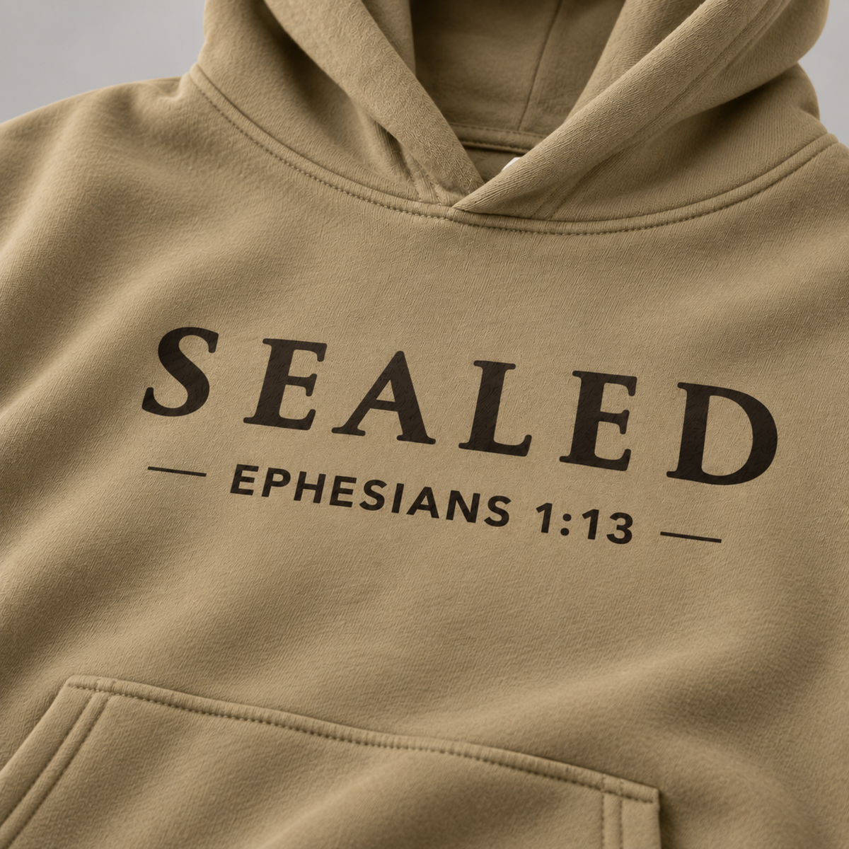 Close-up of the sand SEALED hoodie fabric and black serif SEALED print with Ephesians 1:13 beneath, showing the garment's texture and chest design.
