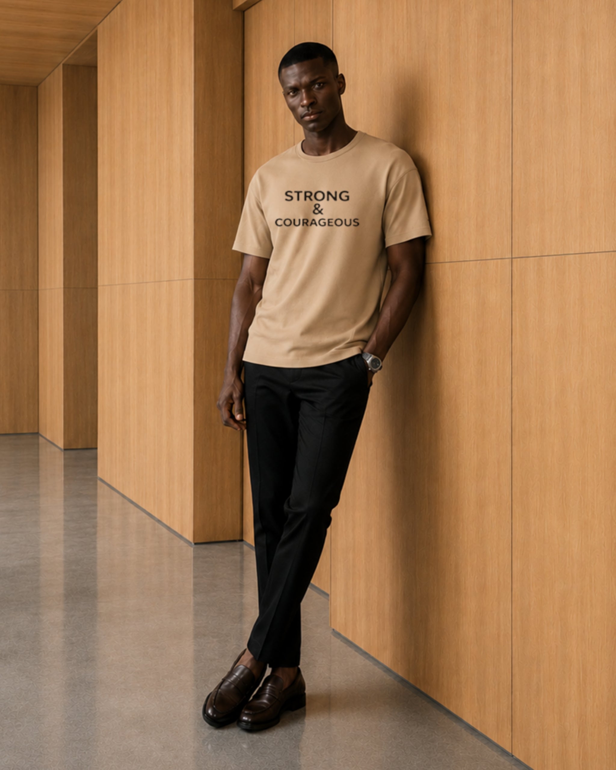 Man wearing a beige t-shirt with text, standing against a wooden wall.