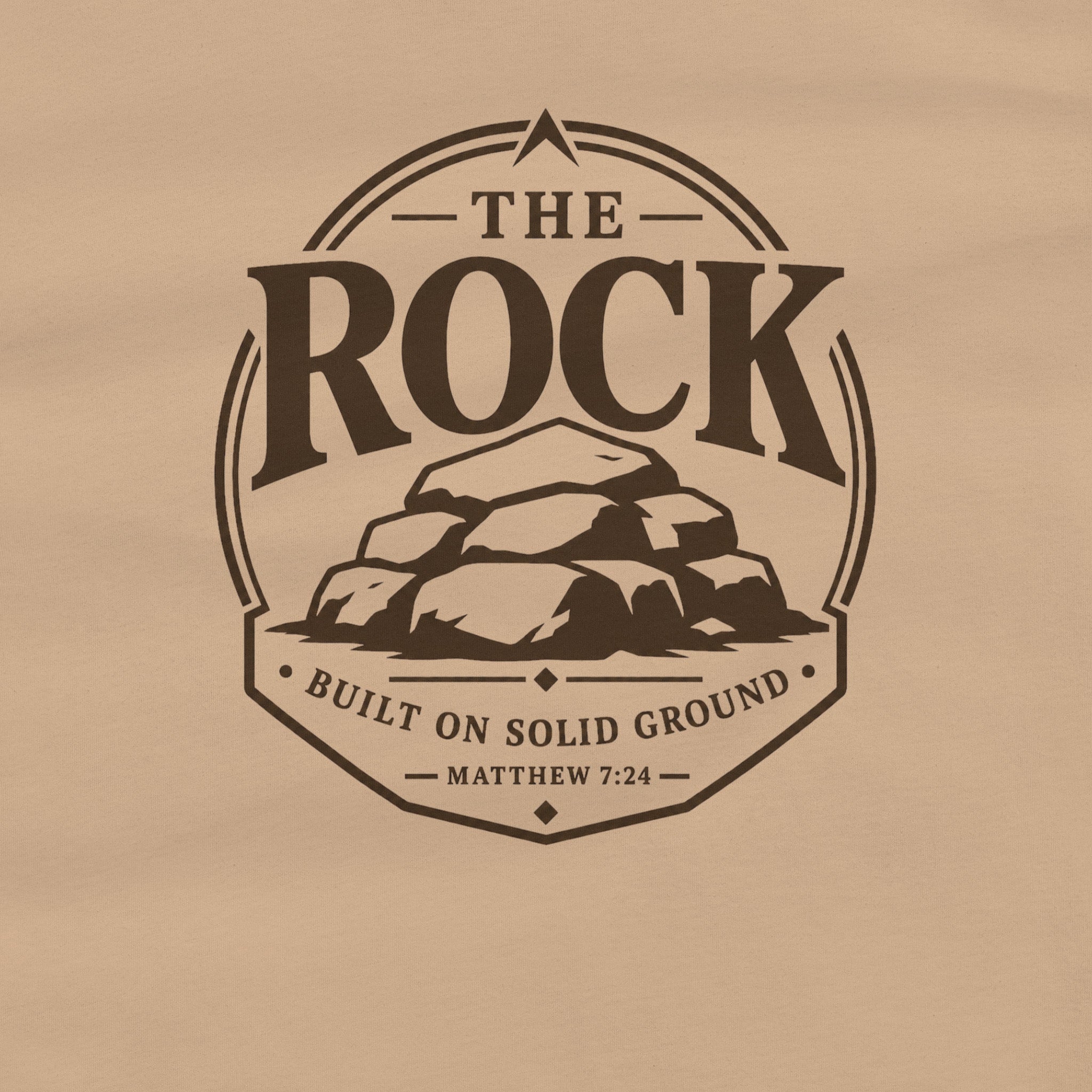 A tan fabric surface featuring a dark brown printed graphic with the words 'THE ROCK BUILT ON SOLID GROUND MATTHEW 7:24' surrounding an illustration of stacked rocks.
