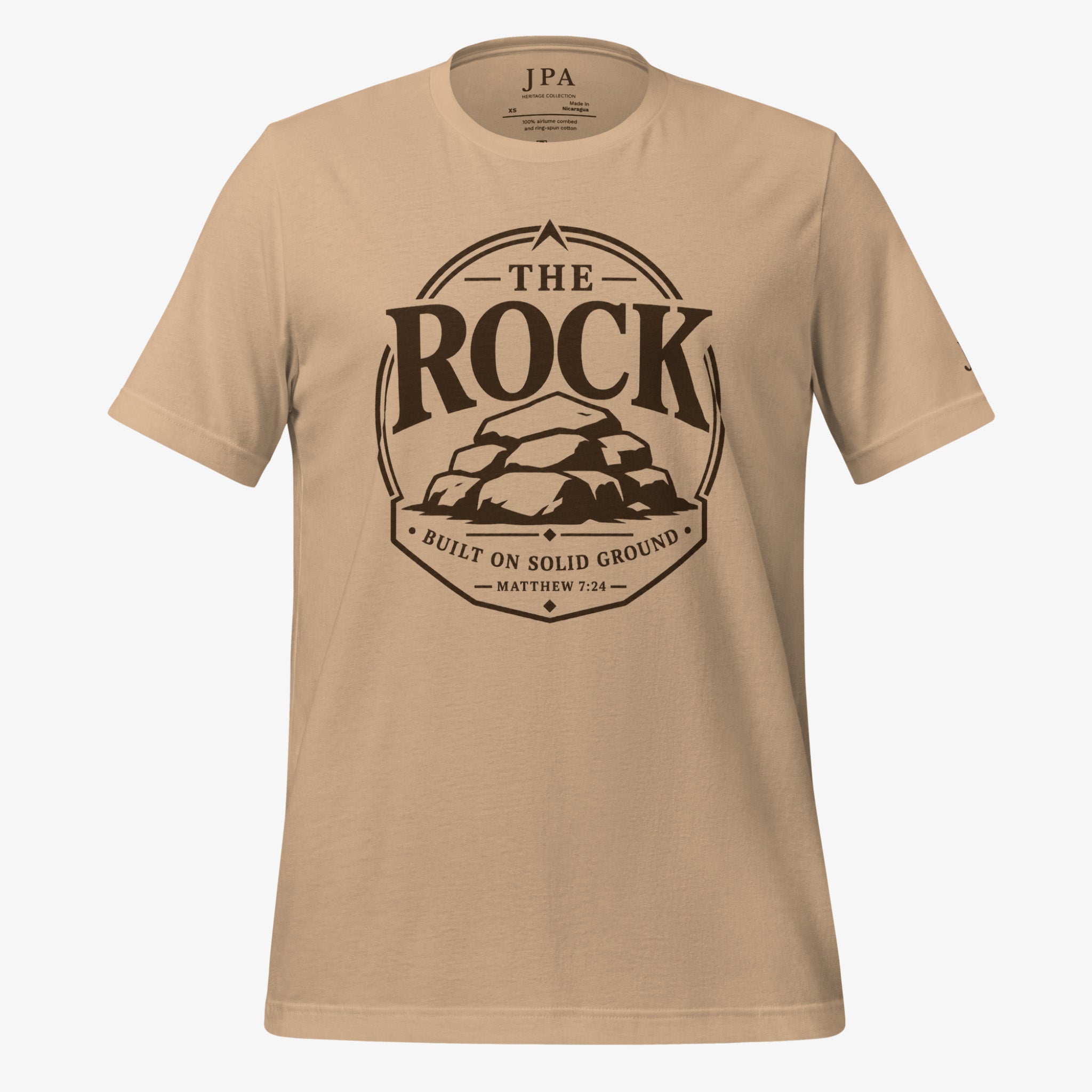 A beige crewneck t-shirt with a dark brown graphic print on the front reading 'THE ROCK BUILT ON SOLID GROUND MATTHEW 7:24' around an illustration of rocks.