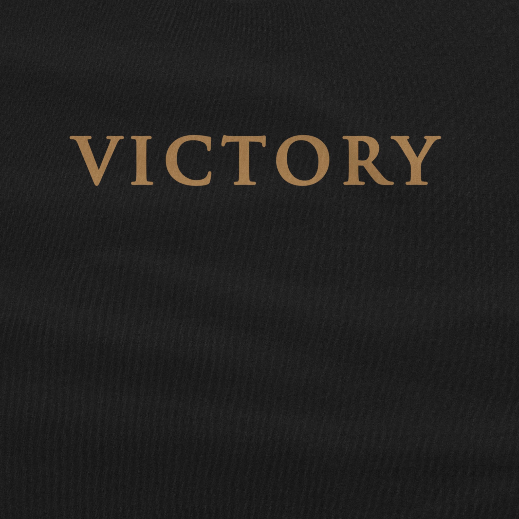 A close-up of a black garment, likely a t-shirt, featuring the word 'VICTORY' printed in a serif gold font across the chest.