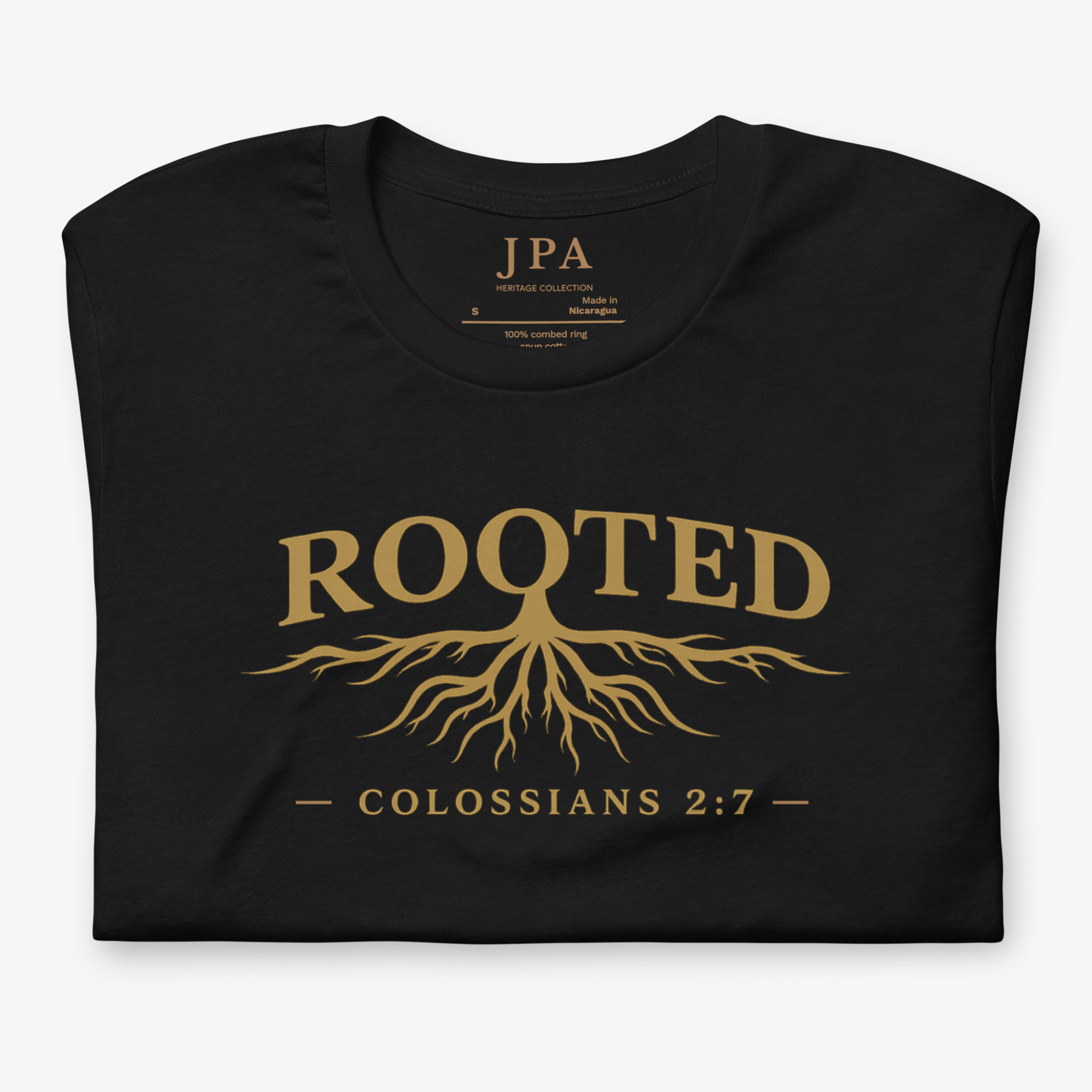 A folded black t-shirt with a gold graphic print on the front. The design features the word 'ROOTED' in a serif font above a stylized tree root system, with the text '— COLOSSIANS 2:7 —' printed below.