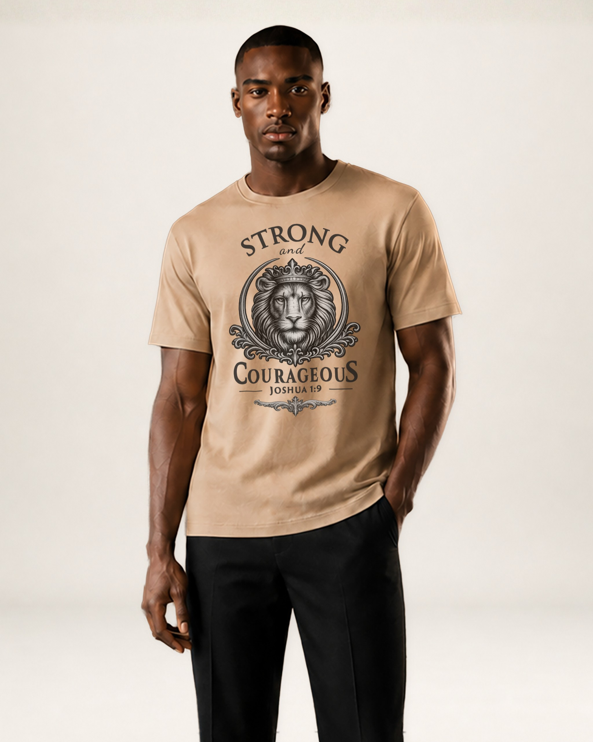 A man modeling a beige crewneck t-shirt with a black graphic print of a lion and the words 'STRONG and COURAGEOUS LONDON' on the front, paired with black trousers, against a light beige studio background.