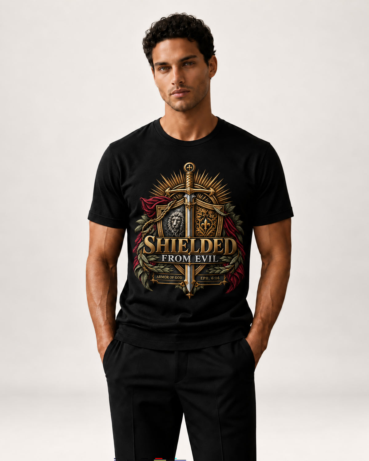 A man modeling a black short-sleeve graphic t-shirt with a detailed medieval knight design featuring a sword, shield, and the text 'SHIELDED FROM EVIL'.