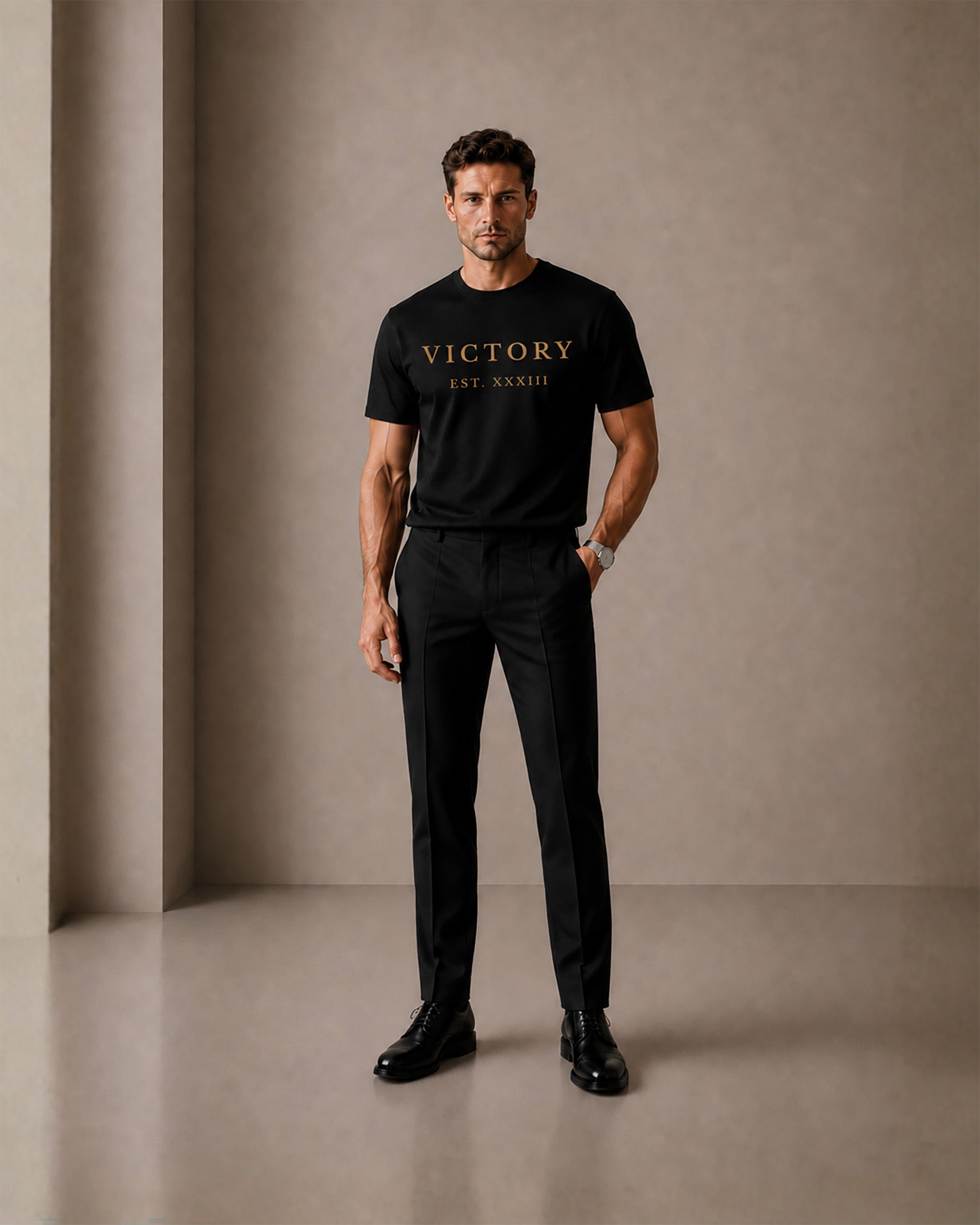 Man wearing a black t-shirt with 'VICTORY' text in gold, standing against a beige wall.