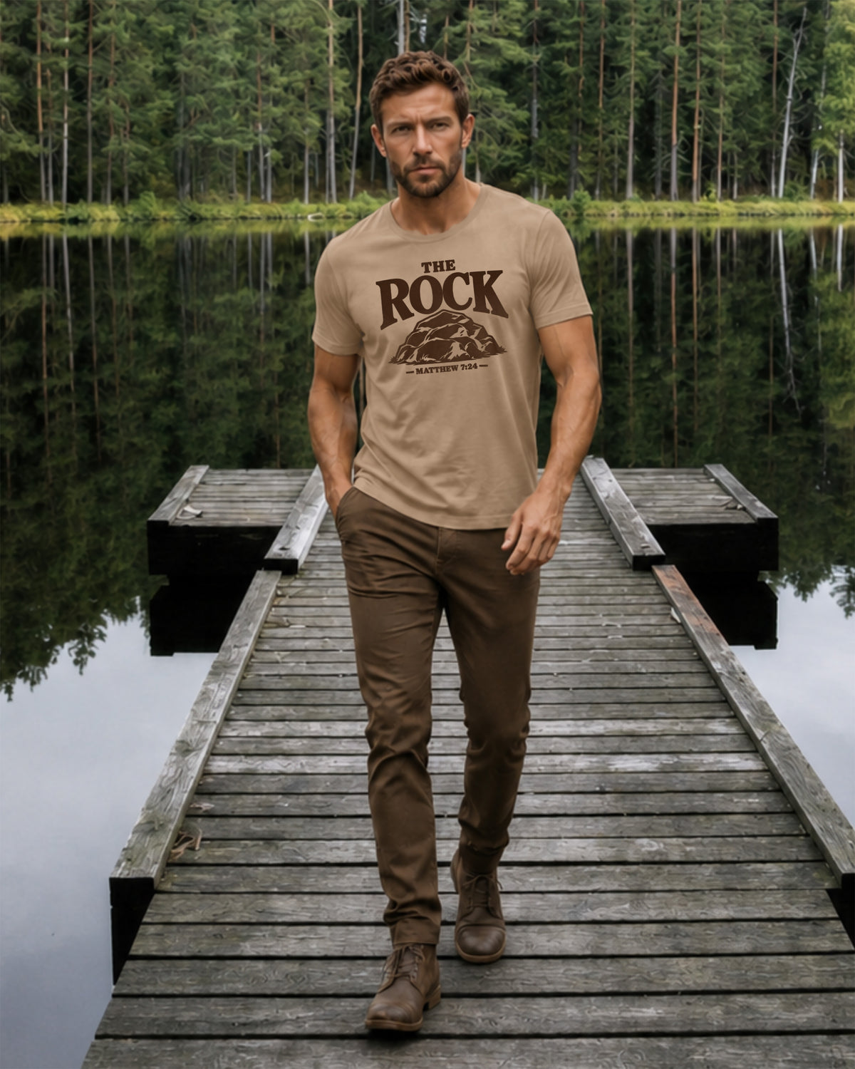A man walking on a wooden dock by a calm lake, wearing a tan crew-neck t-shirt with a dark brown graphic that reads 'THE ROCK' and 'MOSCOW, RUSSIA'.
