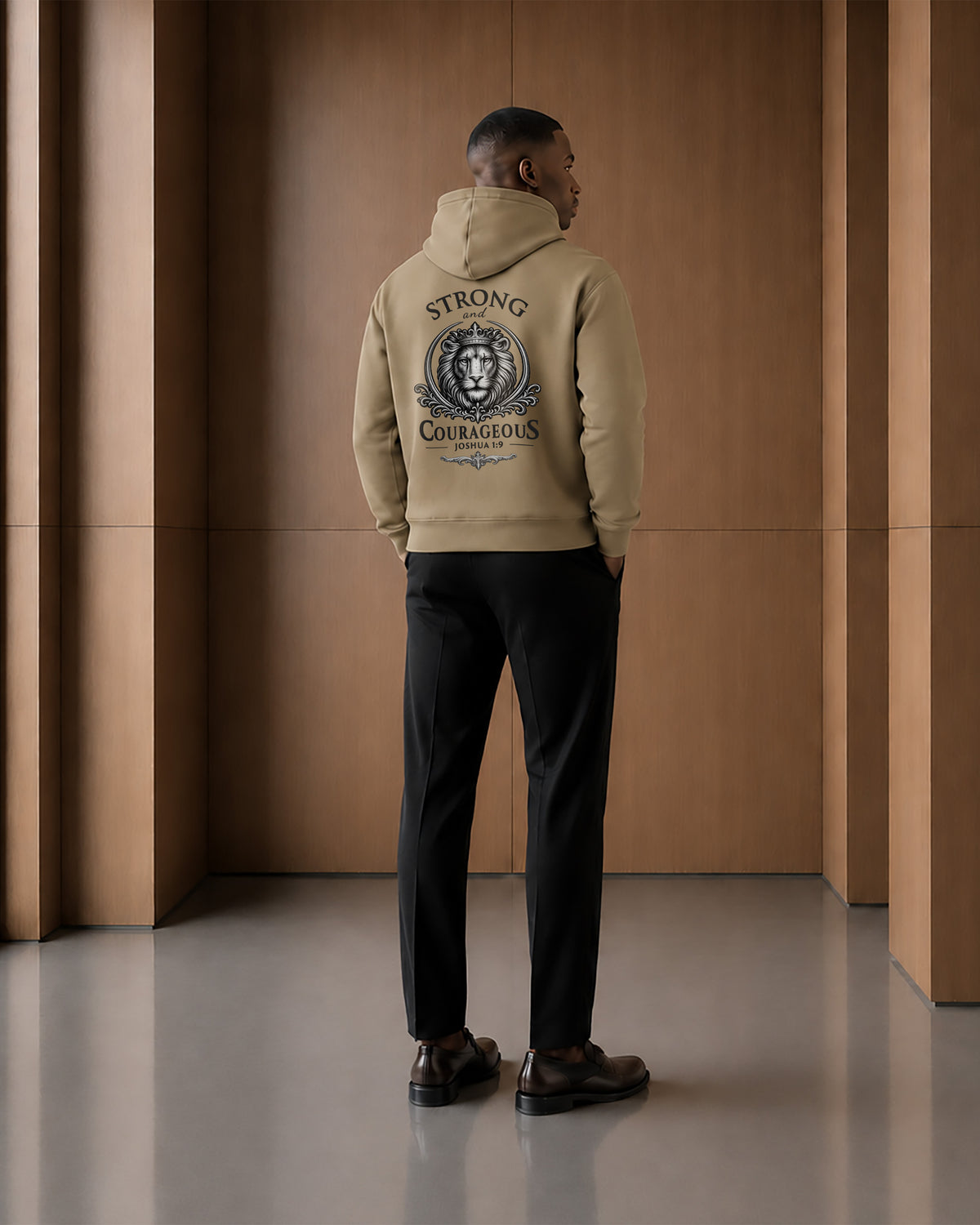 Back view of a model wearing the Strong & Courageous sand hoodie, featuring the large crowned lion illustration and Joshua 1:9 design.