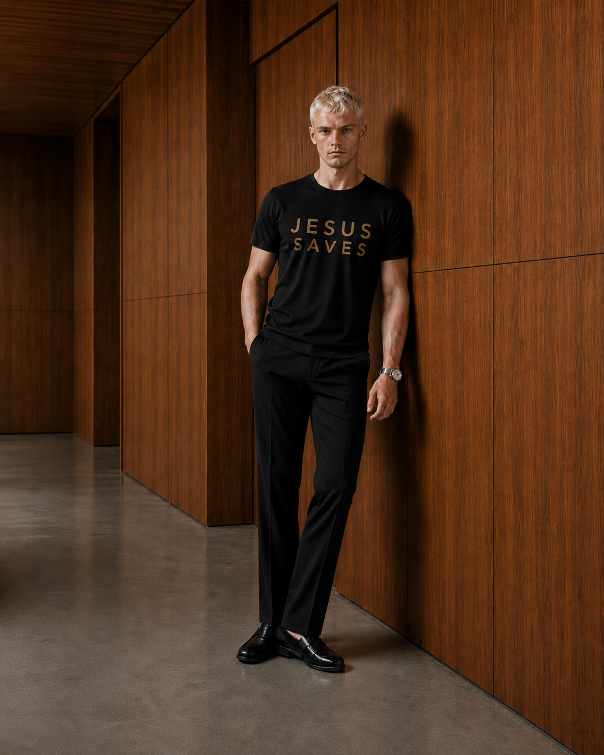 Man wearing a black t-shirt with 'JESUS SAVES' text in a modern indoor setting.