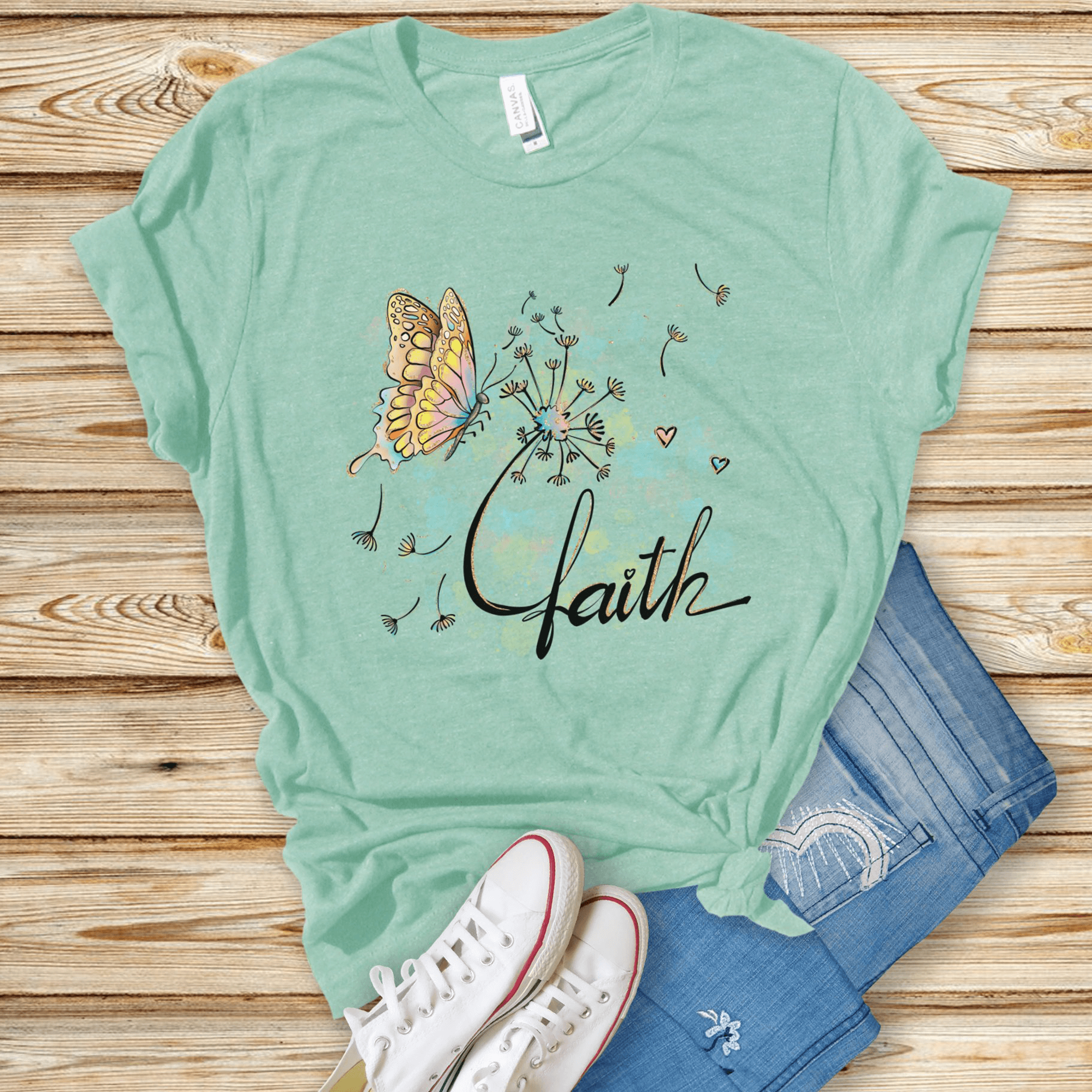 T-Shirts & TopsElevate your wardrobe with this beautifully artistic T-shirt featuring a delicately illustrated butterfly and dandelion with whimsical watercolor accents. The word "faith" is elegantly scripted, adding a touch of inspiration to your day. Pe