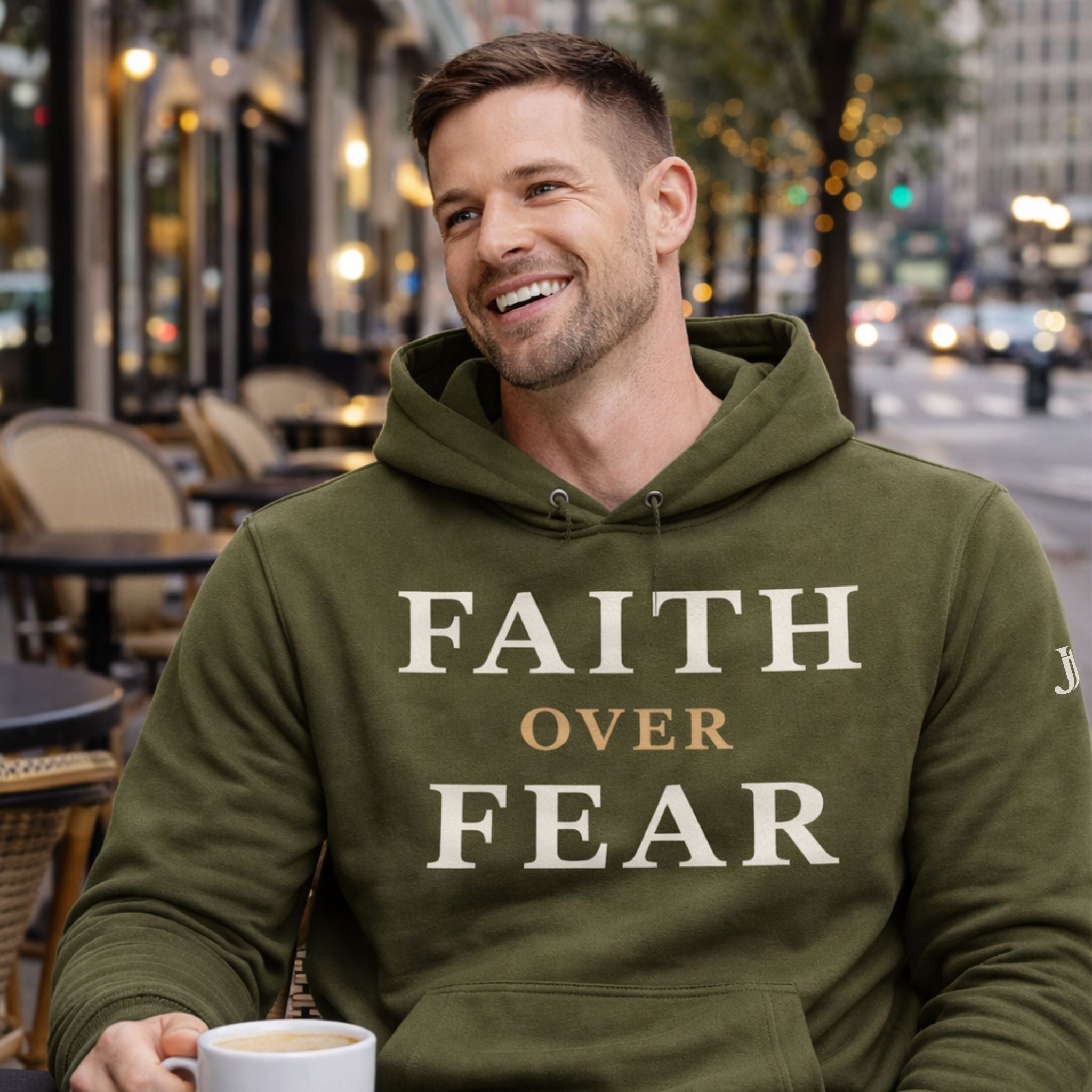 Man wearing a green hoodie with 'Faith Over Fear' text, holding a coffee cup outdoors.