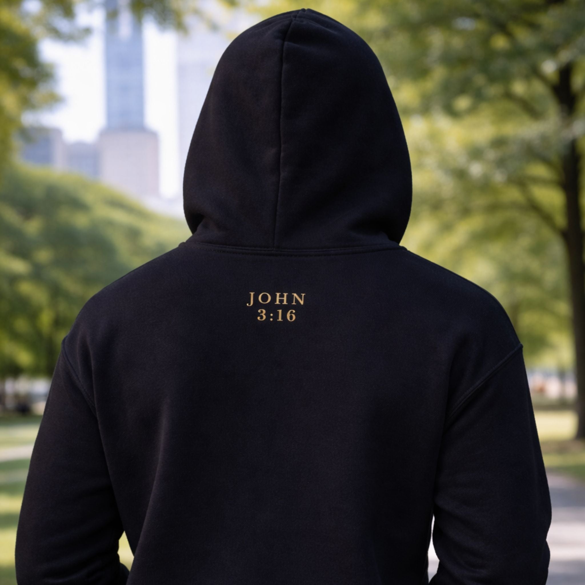 Person wearing a black hoodie with 'JOHN 3:16' text outdoors.