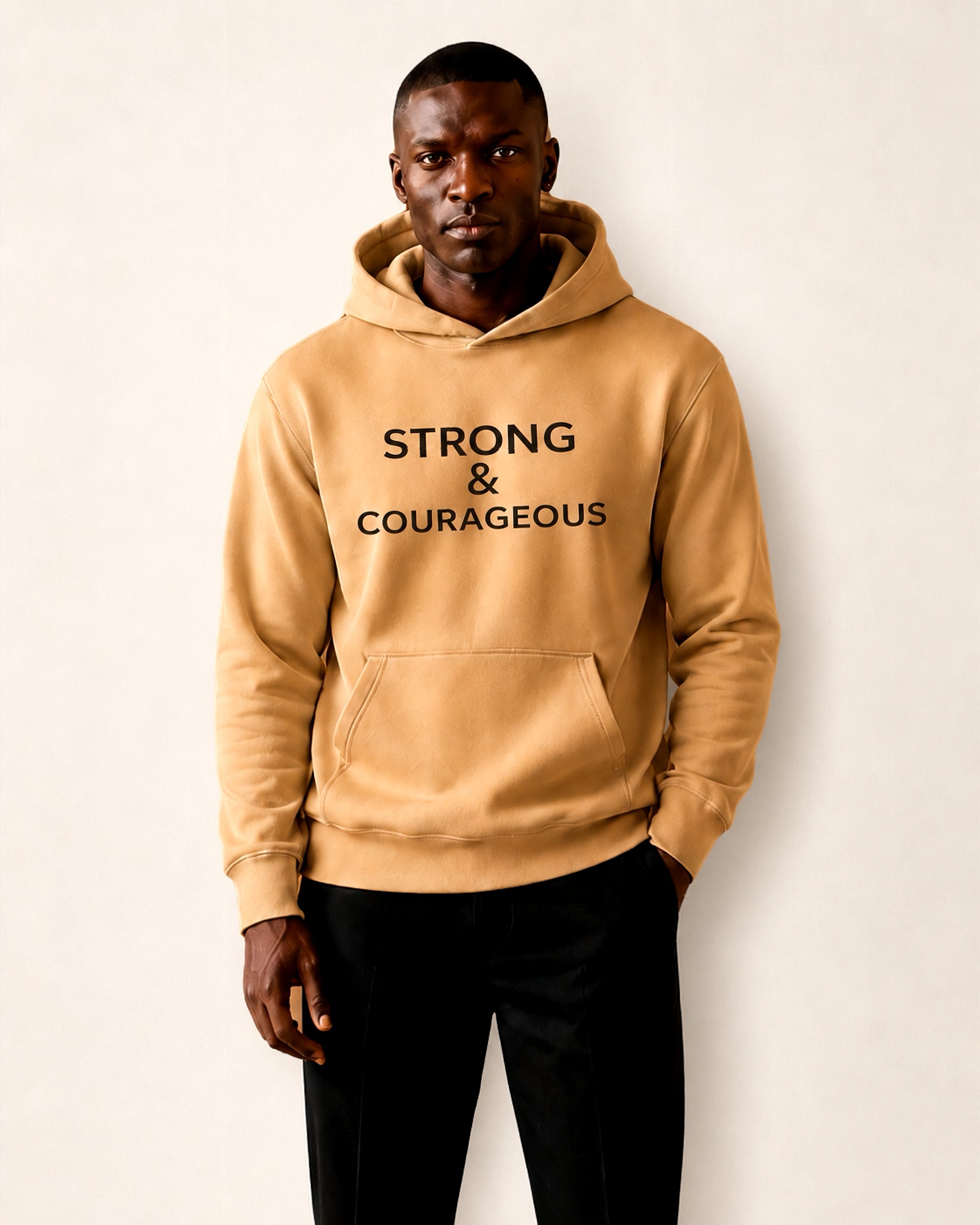 Man wearing a tan hoodie with 'STRONG & COURAGEOUS' text on a plain background