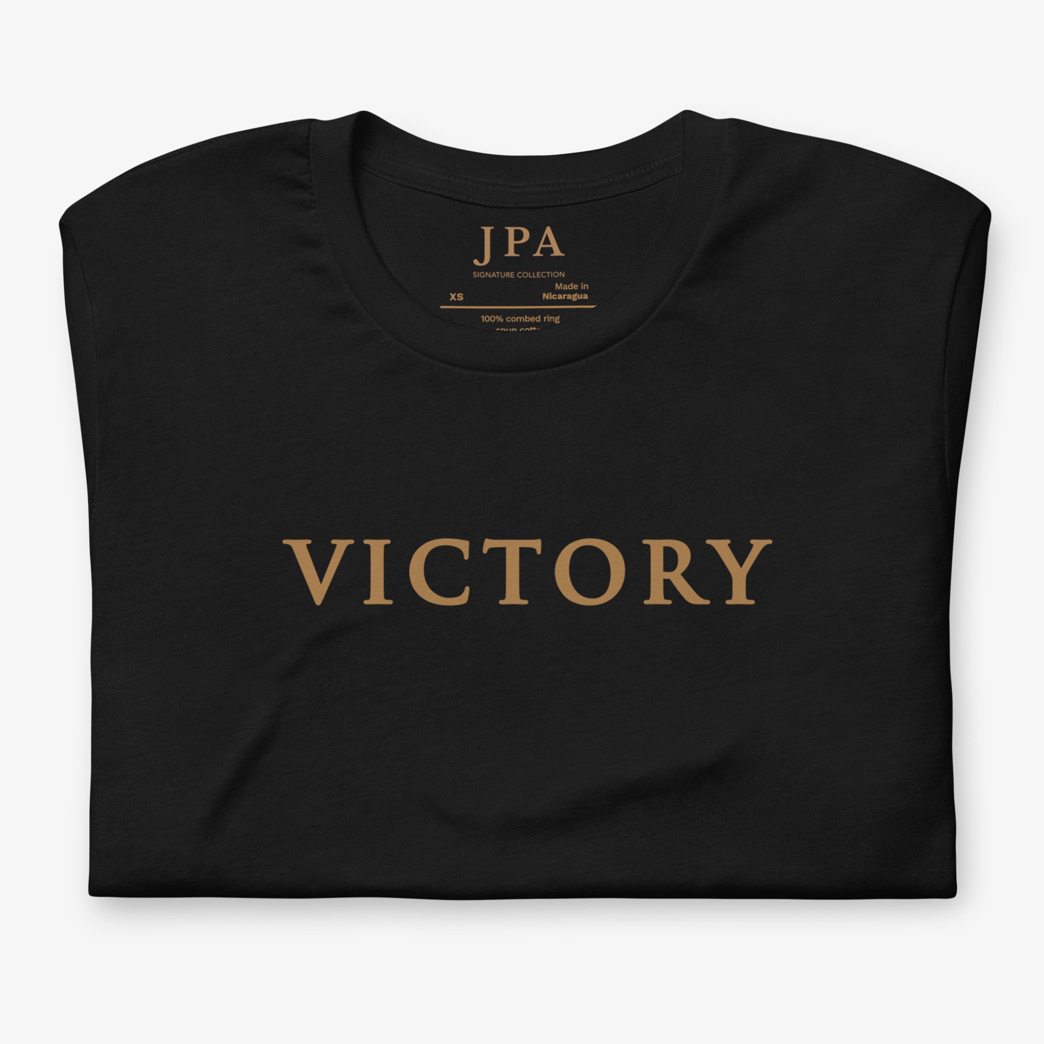 A folded black short-sleeve t-shirt with 'VICTORY' printed in gold across the chest and 'JPA' printed inside the collar, shown on a light gray background.