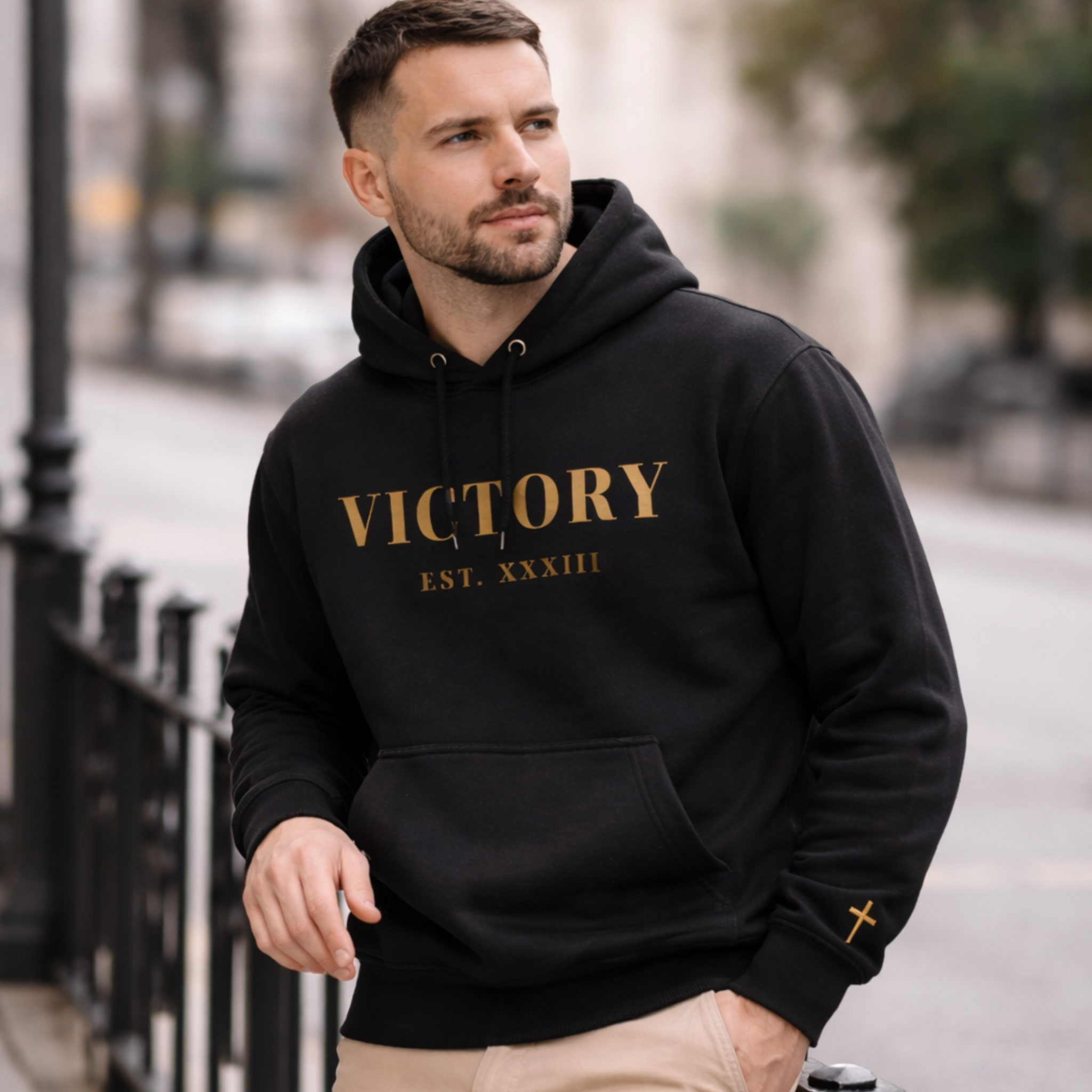 Man wearing a black hoodie with 'VICTORY EST. XXXIII' text outdoors.