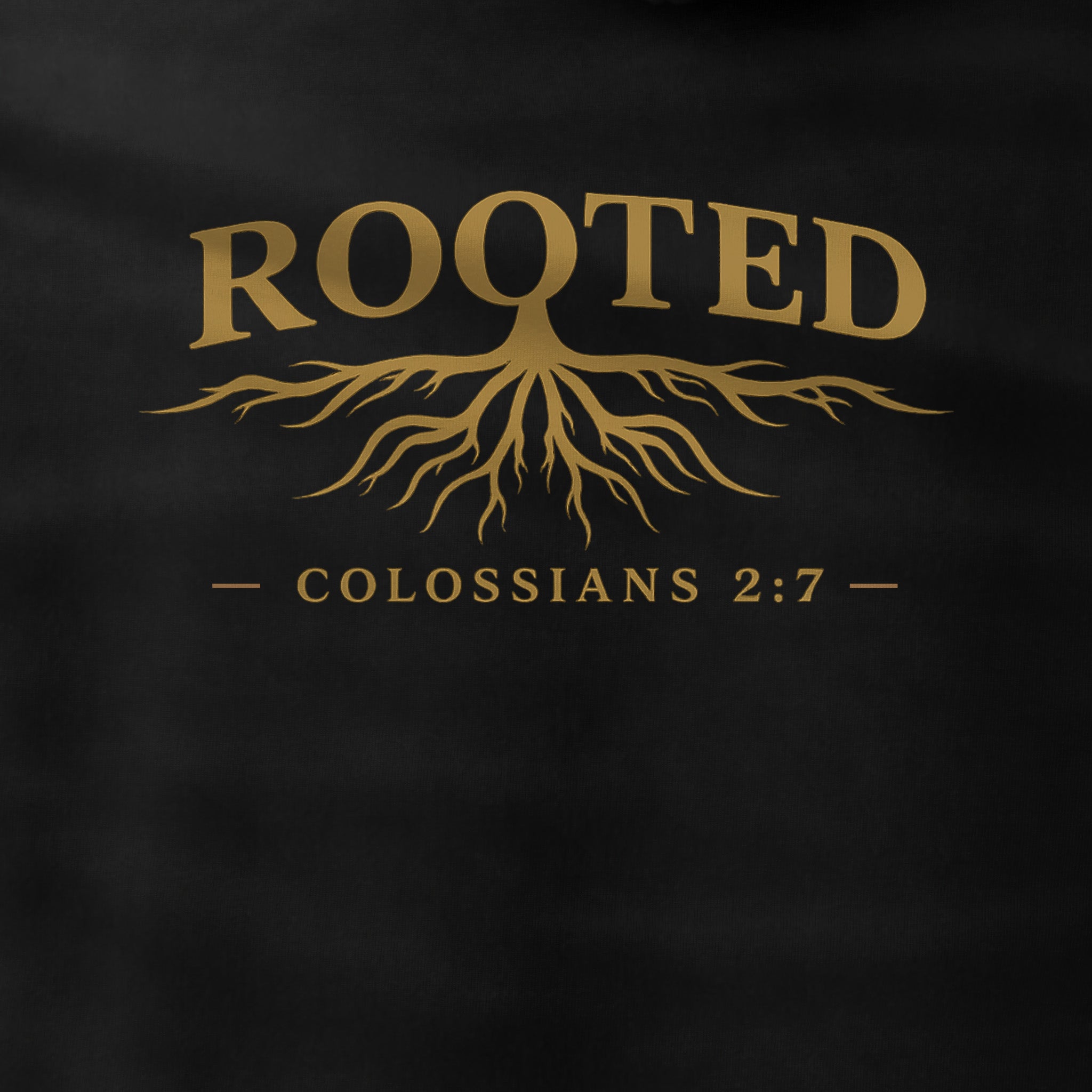 A close-up of a black garment featuring a gold graphic print with the word 'ROOTED' above a tree root design and the text 'COLOSSIANS 2:7'.