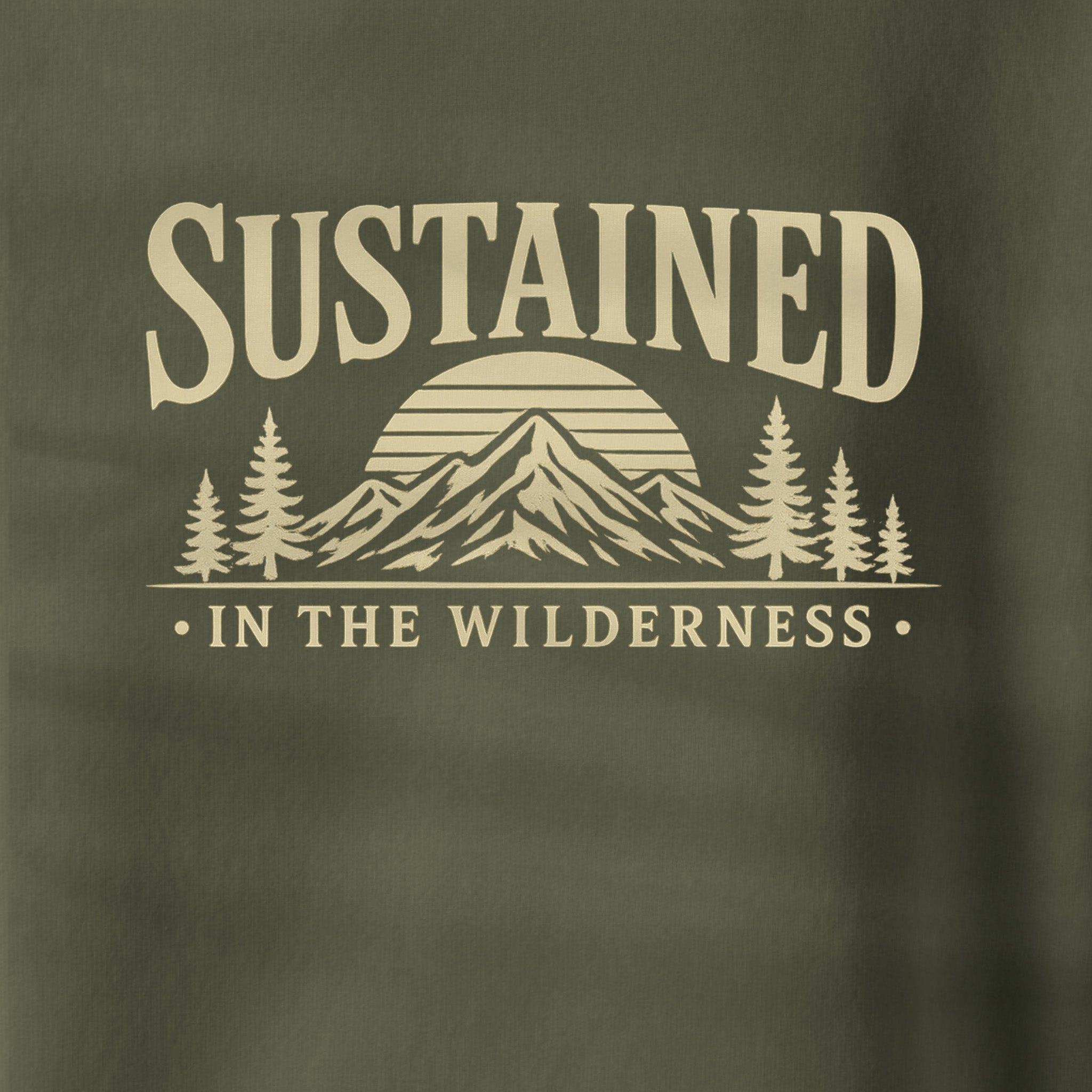 Close-up of a dark olive green fabric with a beige printed graphic reading 'SUSTAINED IN THE WILDERNESS' above a mountain, sun, and pine tree design.