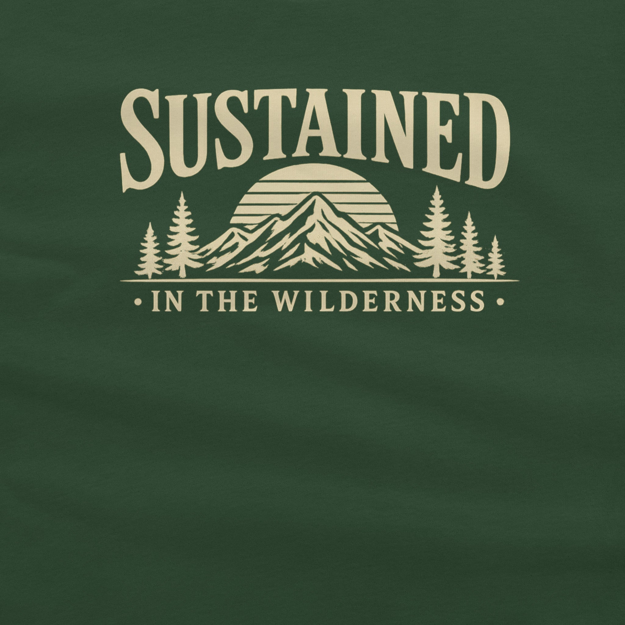 A close-up of a dark green fabric surface with a cream-colored graphic print reading 'SUSTAINED IN THE WILDERNESS' above a mountain and pine tree illustration.