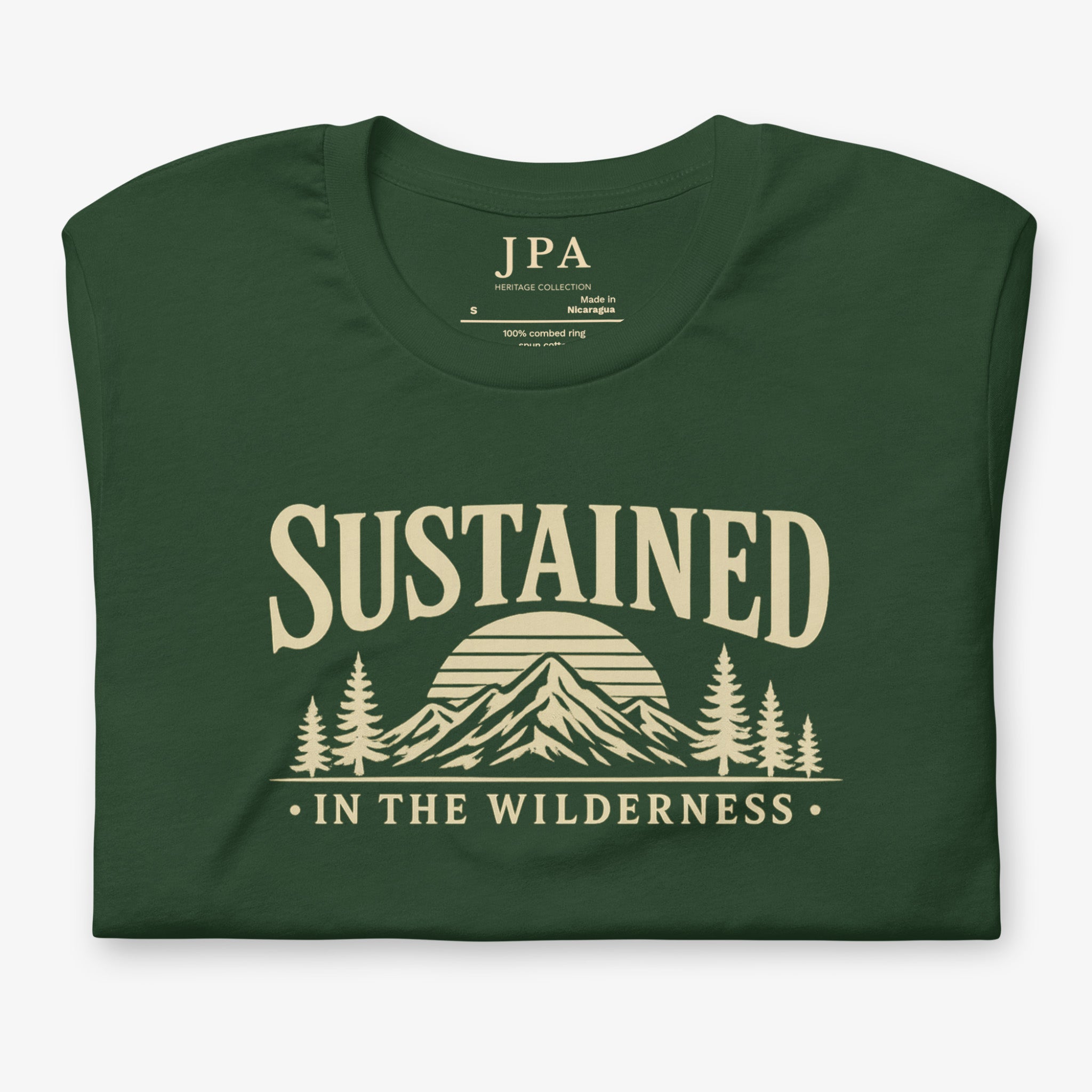 A dark forest green folded t-shirt with a beige graphic print on the front. The graphic features the word 'SUSTAINED' above an illustration of mountains, a rising sun, and pine trees, with the phrase 'IN THE WILDERNESS' below.