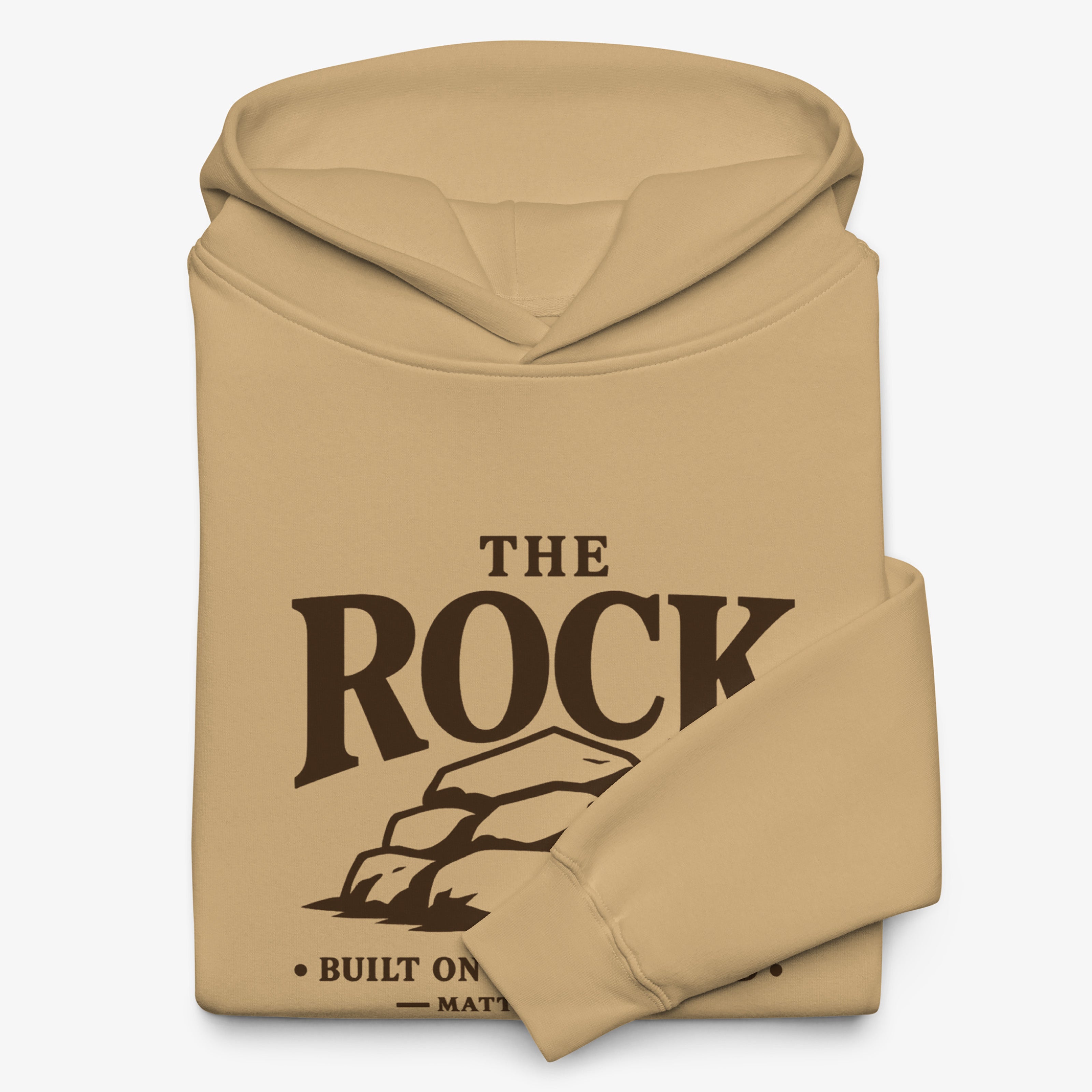 A tan folded hoodie with a dark brown graphic print on the front that reads 'THE ROCK BUILT ON MATTER' with a rock illustration, shown on a light gray background.