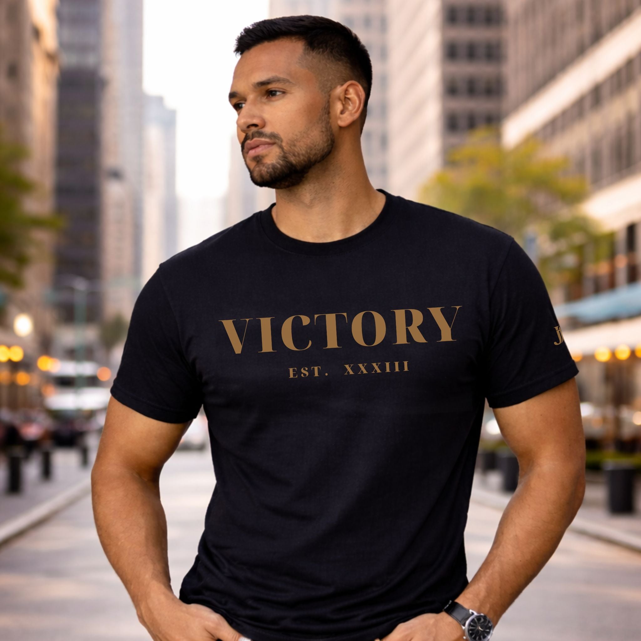 Man wearing a black t-shirt with 'VICTORY EST. XXXVIII' text in an urban setting