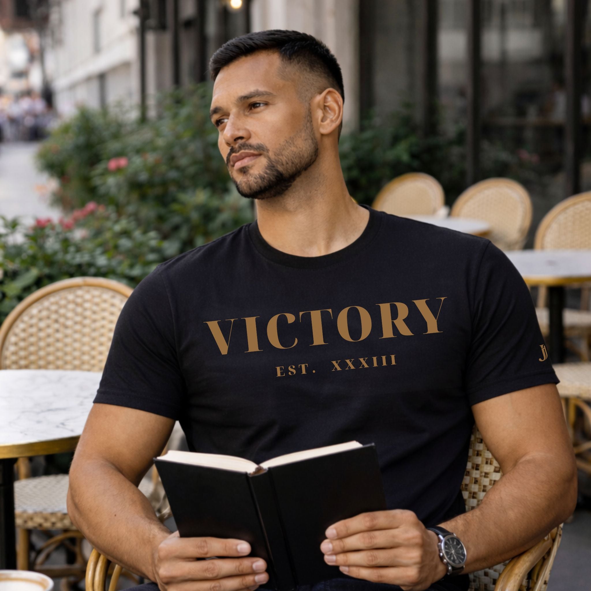 Man wearing a black 'VICTORY' t-shirt sitting outdoors with a book.