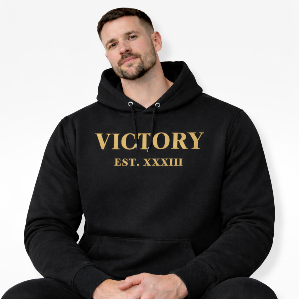 Man wearing a black hoodie with 'VICTORY EST. XXXIII' text in gold on a white background